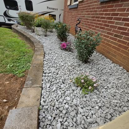Finished landscape bed with white rock, stone edging and new plants along a brick home